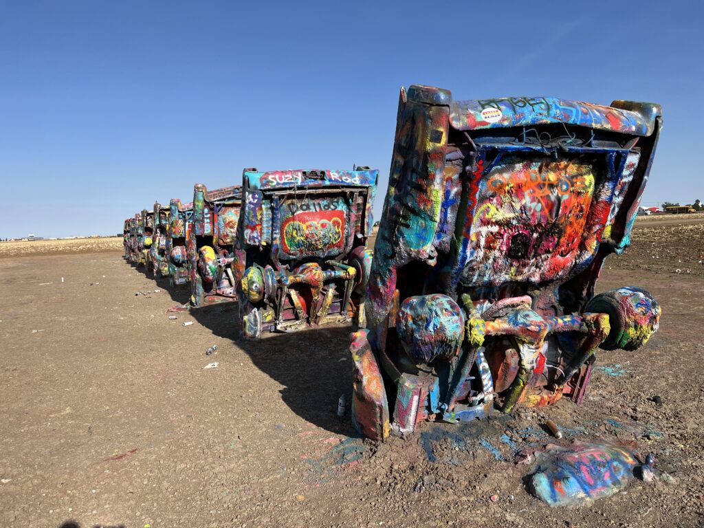 A picture of ten colorfully graffitied Cadillacs buried nose first in a row, one behind the other.