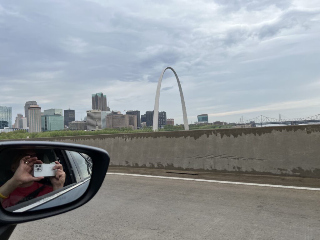 A picture of the St. Louis Arch taken from the highway with the city of St. Louis in the background.